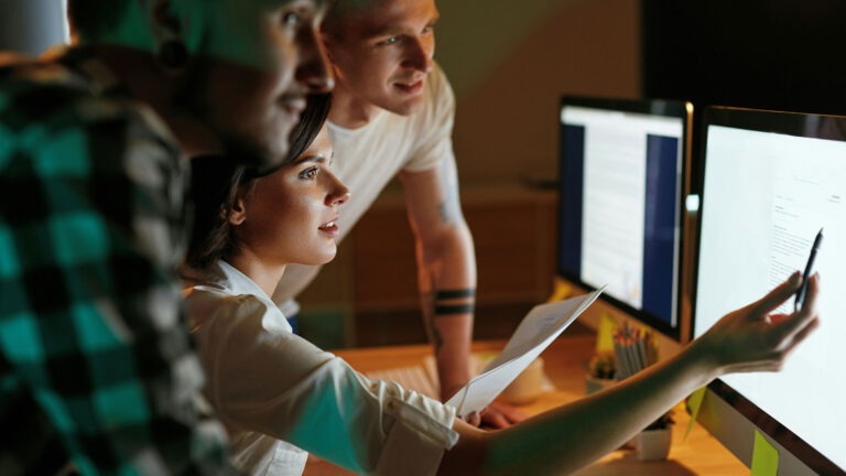 Drei junge Menschen schauen auf einen PC-Monitor und sprechen über Lizenzen.