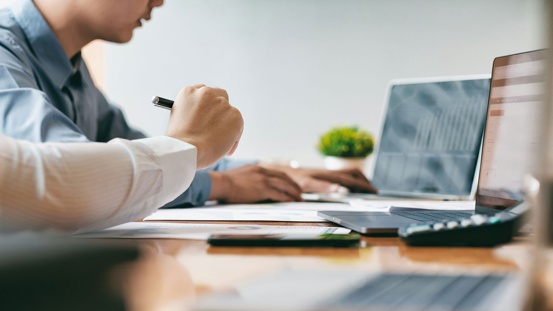 Zwei Personen sitzen am Schreibtisch vor Laptops und Unterlagen und berechnen die Lizenzkosten