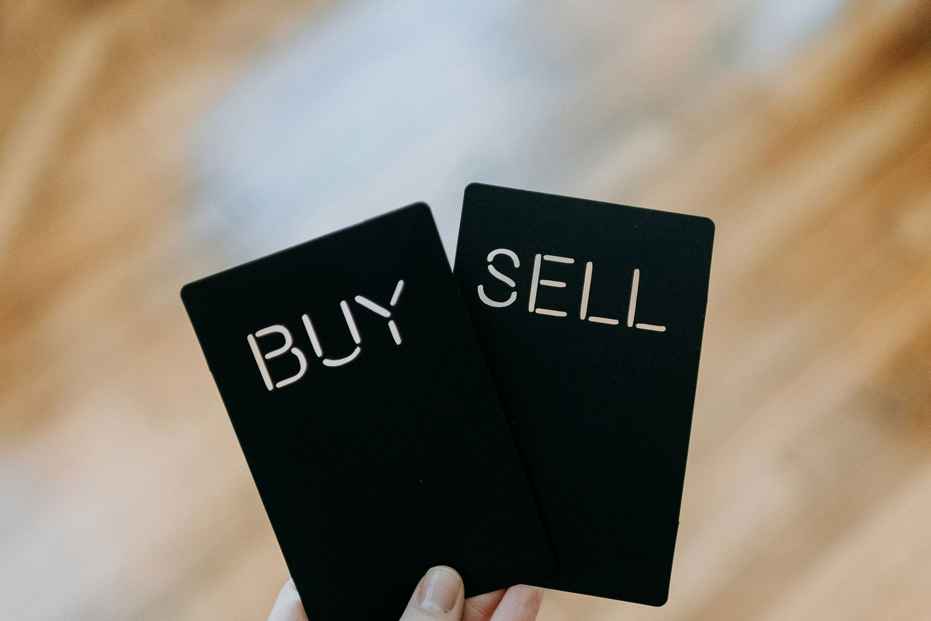 Eine Hand hält zwei Karten hoch. Auf der linken Karte steht 'Buy' oder auf der rechten 'Sell'